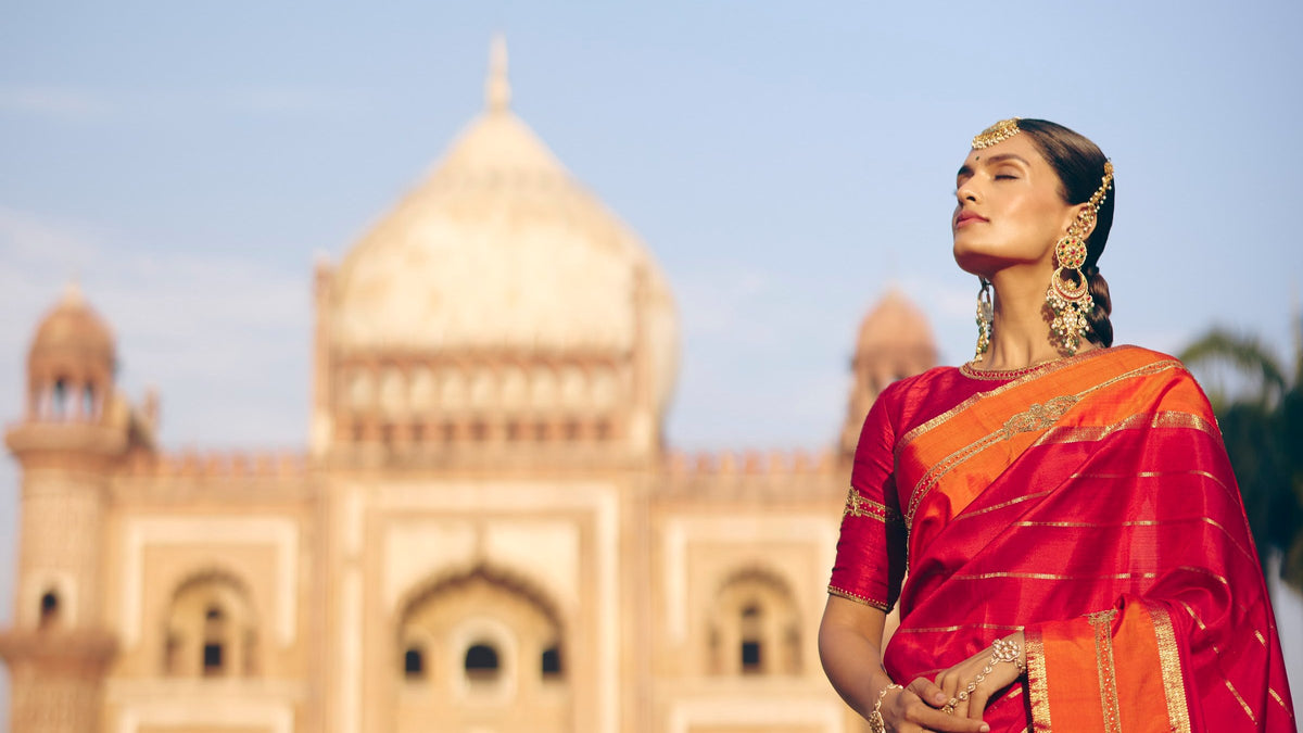 Bride in a red and orange Kanjivaram silk saree before a Mughal monument, The Silk Hour by The Saffron House