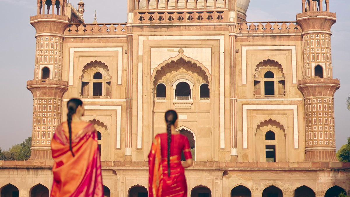 Two women in red and orange Kanjivaram silk sarees before a Mughal tomb, The Silk Hour by The Saffron House