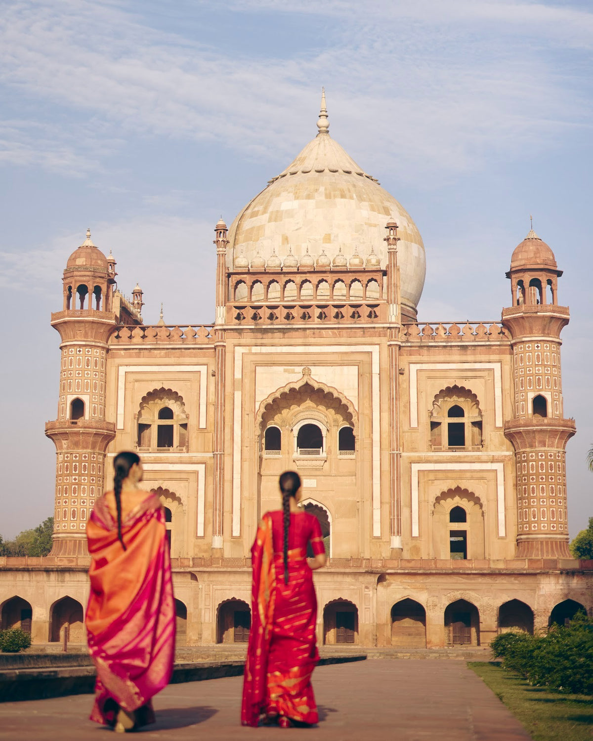 Two women in red and orange Kanjivaram silk sarees before a Mughal tomb, The Silk Hour by The Saffron House